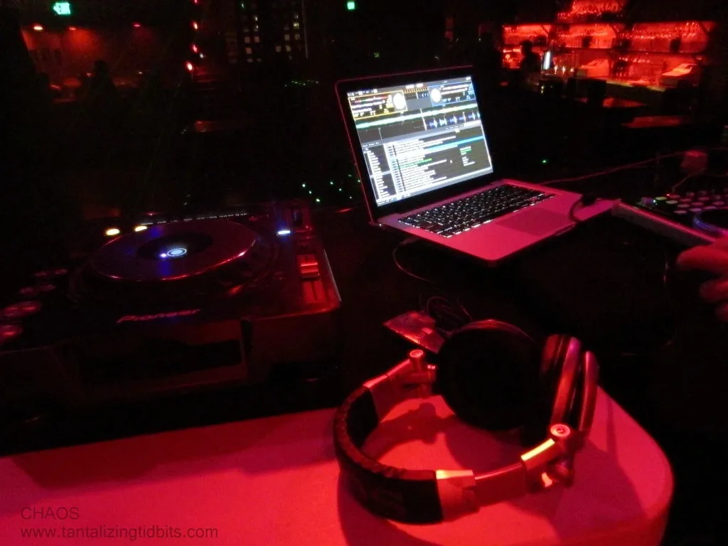 A DJ booth in red light with headphones, a laptop and a turntable
